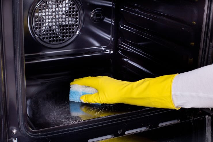 mano con guanto giallo che pulisce il forno